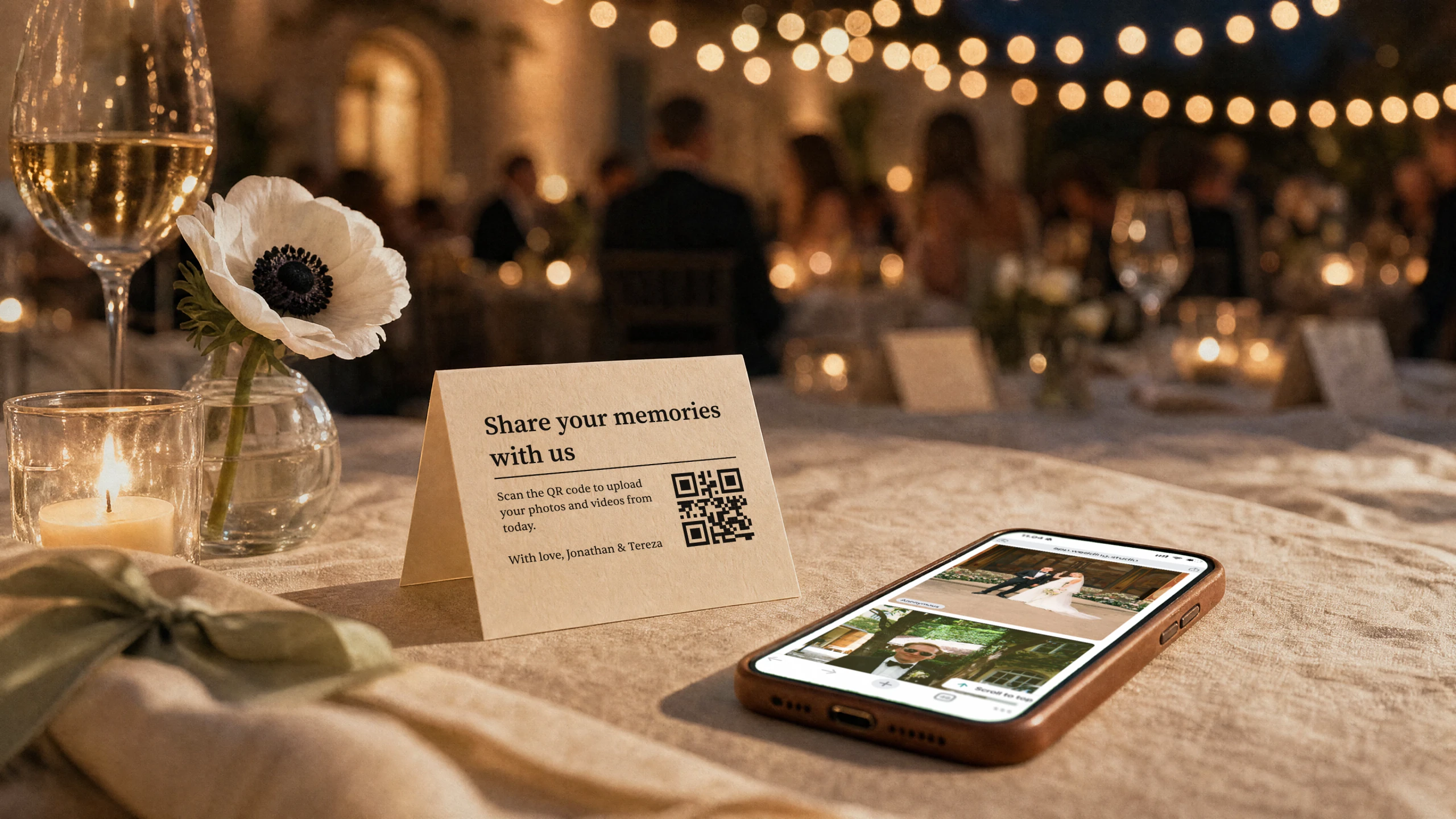 Wedding reception table at dusk with QR table card and phone showing shared guest photos